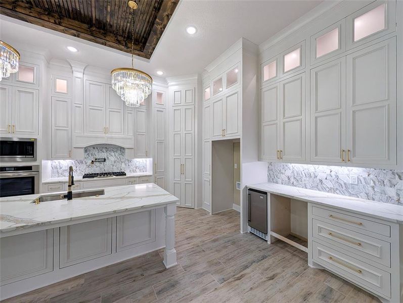 Kitchen with backsplash, light stone counters, glass insert cabinets, appliances with stainless steel finishes, and pendant lighting
