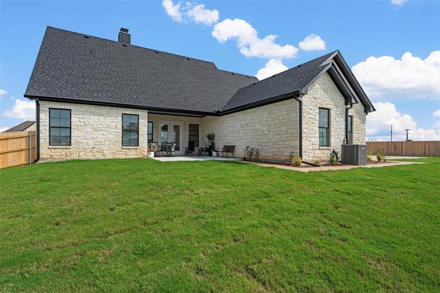 Back of property featuring stone siding, a patio area, a fenced backyard, roof with shingles, and a chimney Back of property featuring stone siding, a patio area, a fenced backyard, roof with shingles, and a chimney