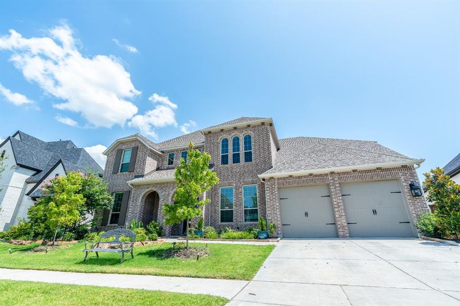 View of front facade with brick siding, driveway, and roof with shingles