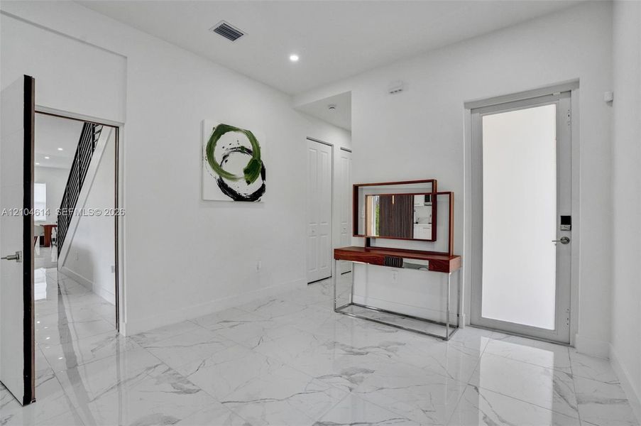 White marble-finish flooring throughout, recessed ceiling lighting, and a white interior door with contemporary hardware