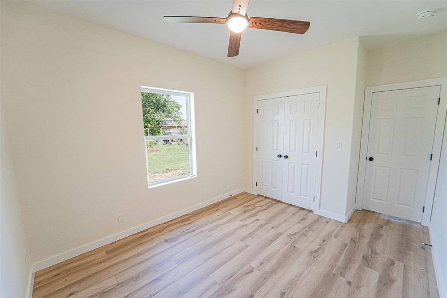 Guest/3rd Bedroom-Interior space featuring light wood-finish flooring, a ceiling fan with integrated lighting, a window with a white frame, and a spacious closet with double doors