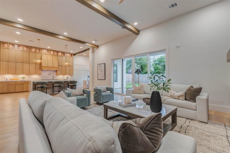 Spacious living room designed for connection, featuring beam-accented ceilings, oversized sliders, and a natural flow into the kitchen and dining spaces.