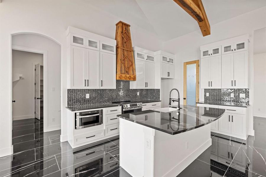 Kitchen with glass insert cabinets, beam ceiling, tasteful backsplash, and dark stone counters Kitchen with glass insert cabinets, beam ceiling, tasteful backsplash, and dark stone counters