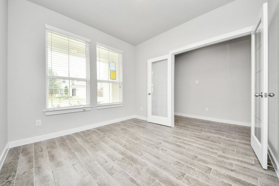 Experience the perfect blend of sophistication and warmth in this home office, boasting elegant wood-look tile flooring and flooded with natural light from expansive windows and French doors. Sample photo of completed home with similar floor plan. Actual colors and selections may vary.