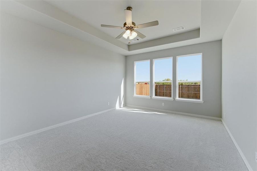 Empty room featuring carpet, a ceiling fan, and a raised ceiling