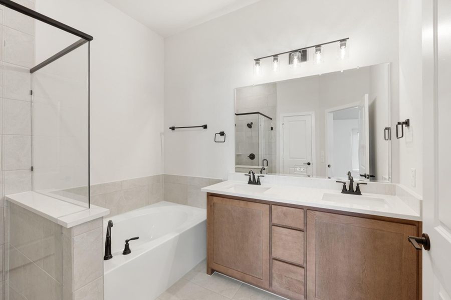 Bathroom with double sink vanity, soaking tub, and glass shower with black fixtures and tile floors