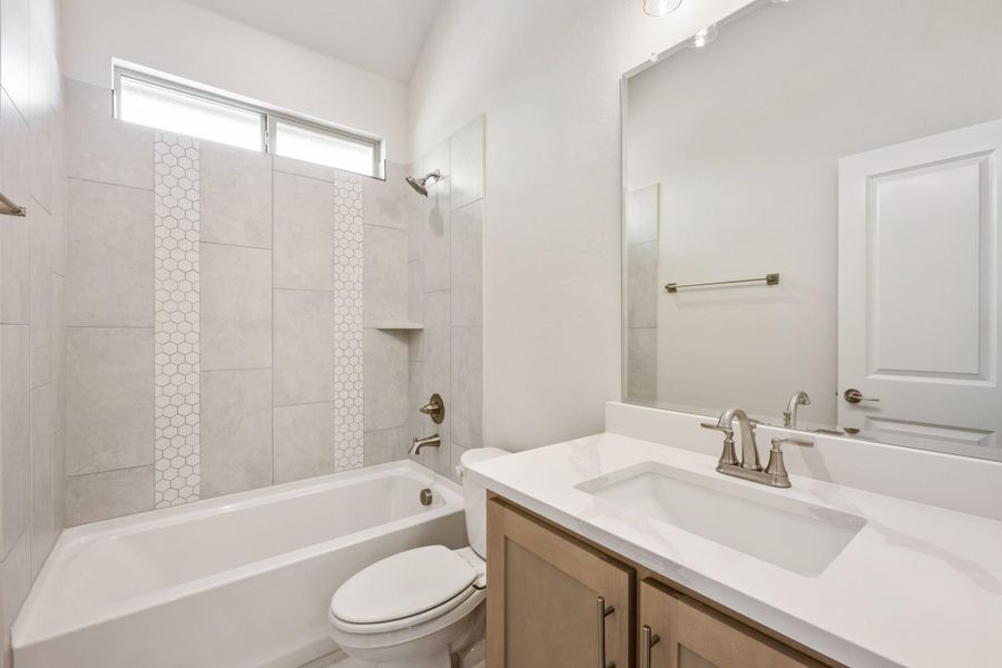 Bathroom with tiled tub-shower combo, wood vanity with white countertop, and vaulted ceiling