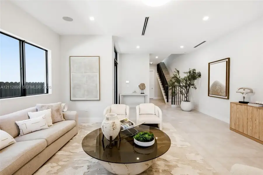 Open-concept interior featuring large-format tile flooring, recessed lighting, and a staircase with a black metal railing