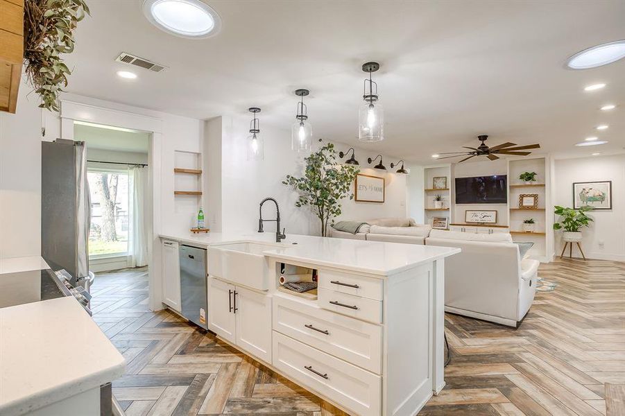 Kitchen featuring white cabinets, parquet flooring, built in shelves, stainless steel dishwasher, and decorative light fixtures