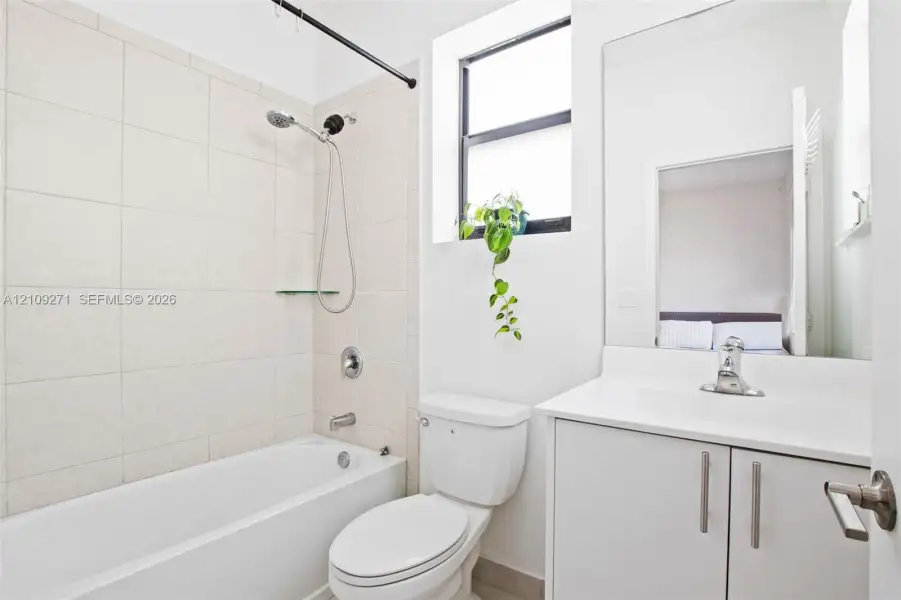 Bathroom featuring a white vanity cabinet with a integrated countertop, large wall-mounted mirror, ceramic-tiled shower surround, and a handheld shower fixture