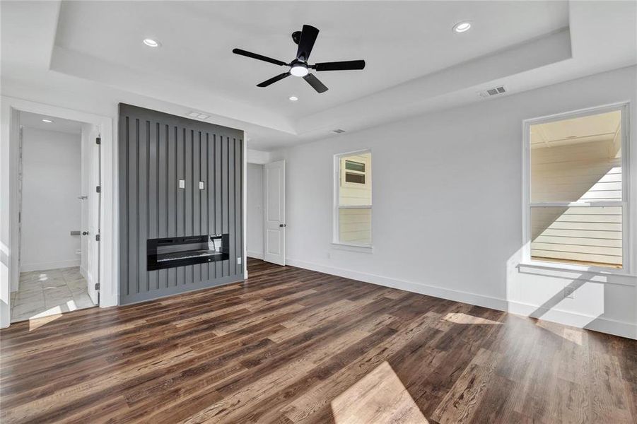 Unfurnished living room featuring a tray ceiling, ceiling fan, dark wood-type flooring, a glass covered fireplace, and recessed lighting