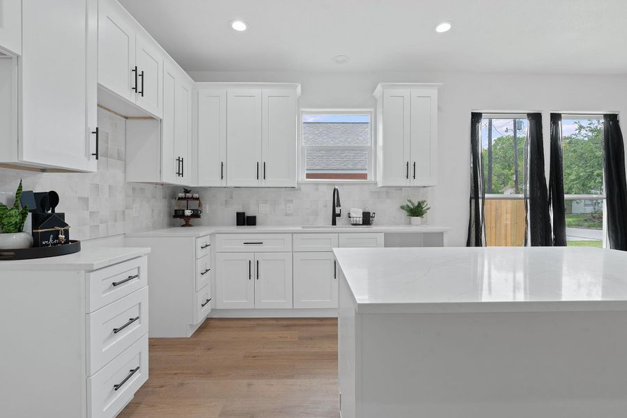 Kitchen featuring backsplash, light wood finished floors, recessed lighting, white cabinets, and light stone countertops