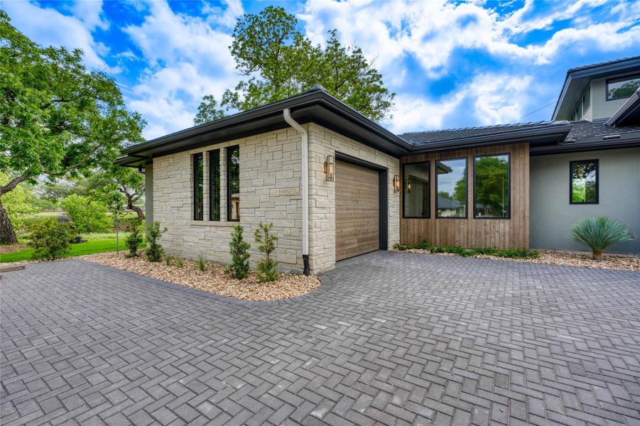 View of side of home featuring an attached garage, decorative driveway, and stone siding