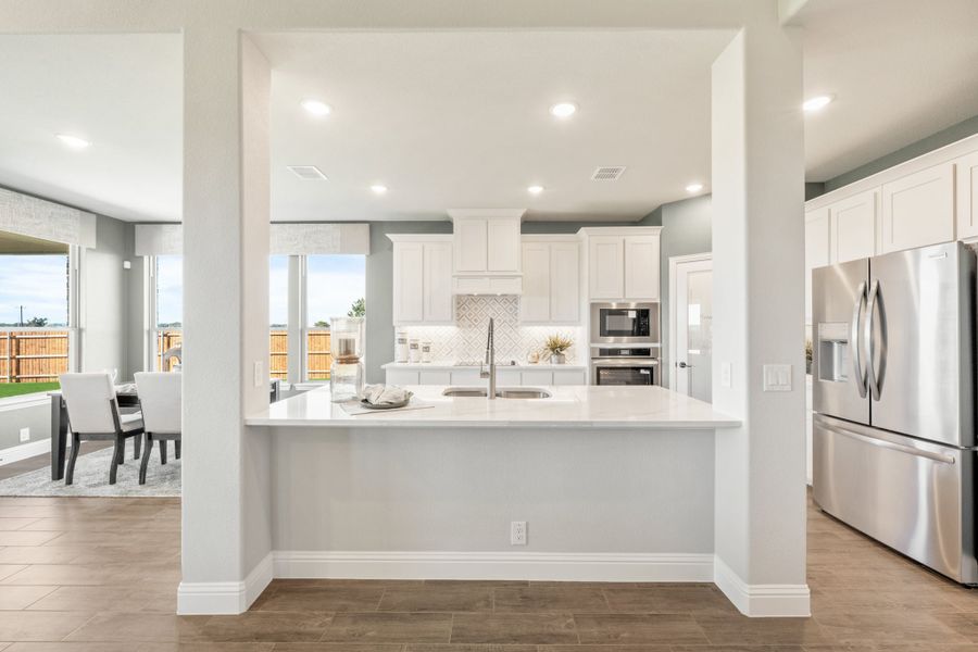 Kitchen with white cabinets, quartz island, stainless steel appliances, and tile backsplash open to dining area