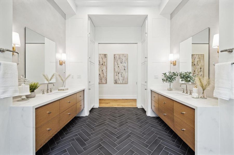 Dual vanities adorned with Kohler under-mount white sinks and white oak cabinetry exude sophistication in this bathroom. Kohler polished nickel faucets add a touch of elegance to the Forza Symphony Quartz waterfall countertops. Against the backdrop of grey plastered accent walls, Visual Comfort lighting sconces provide the perfect ambiance for indulgent self-care routines.