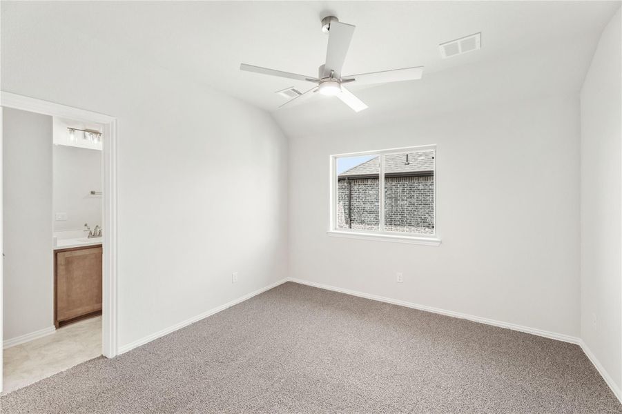 Empty bedroom with vaulted ceiling, ceiling fan, carpet floors, and ensuite bathroom doorway