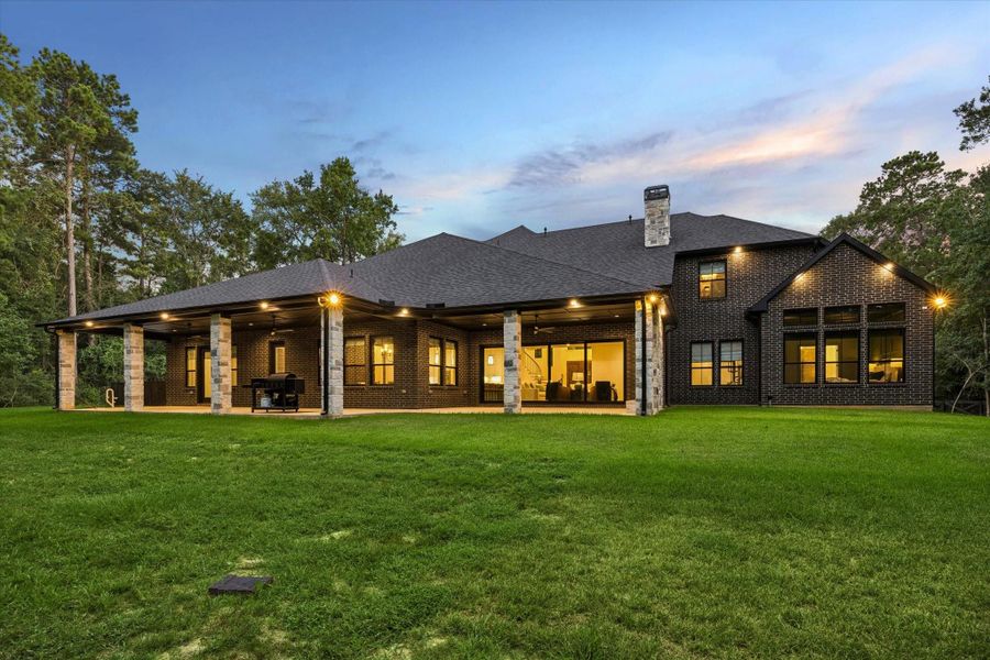As dusk settles, the rear elevation reveals the home's impressive architectural presence. Expansive covered living areas, beautifully landscaped grounds, and timeless design create a private estate equally suited for intimate evenings or grand celebrations.