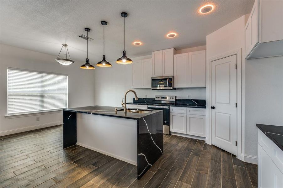 Kitchen featuring an island with sink, appliances with stainless steel finishes, white cabinetry, pendant lighting, and a textured ceiling Kitchen featuring an island with sink, appliances with stainless steel finishes, white cabinetry, pendant lighting, and a textured ceiling