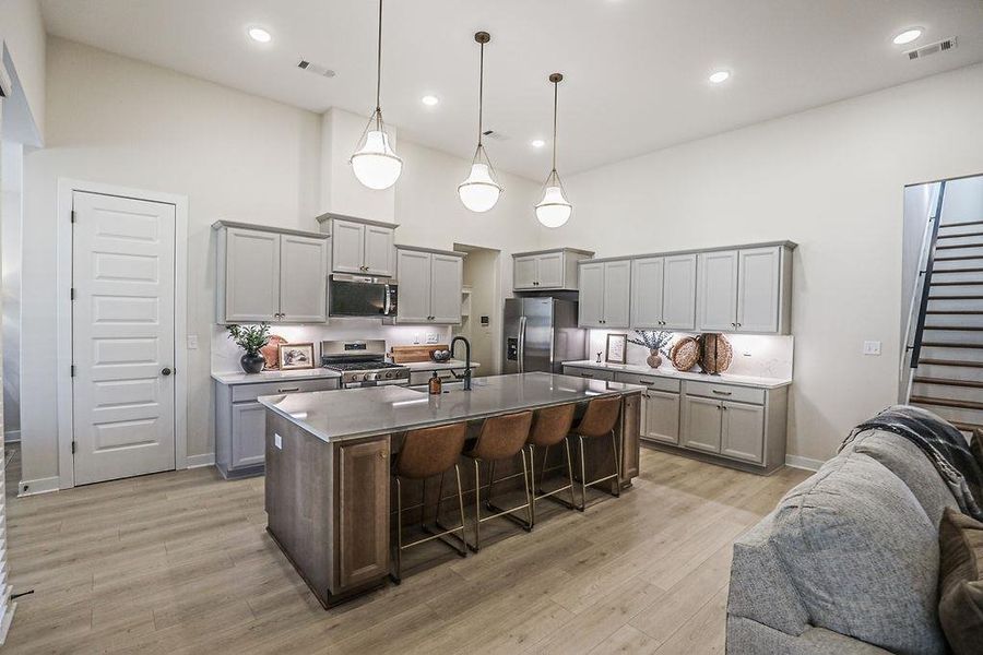 Kitchen featuring a breakfast bar area, gray cabinets, a high ceiling, a center island with sink, and stainless steel appliances