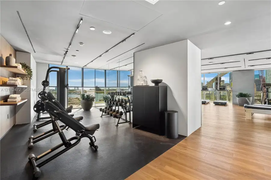 Fitness center featuring floor-to-ceiling windows, wood-finish flooring, rubberized exercise surfacing, recessed lighting, and wall-mounted wooden shelving