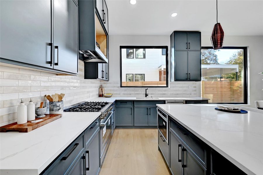 Kitchen with recessed lighting, light stone counters, appliances with stainless steel finishes, pendant lighting, and light wood-style floors