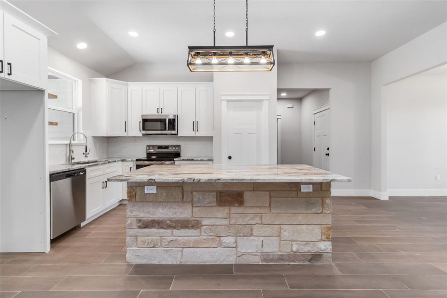 Kitchen featuring a kitchen island, sink, white cabinets, stainless steel appliances, and light stone countertops