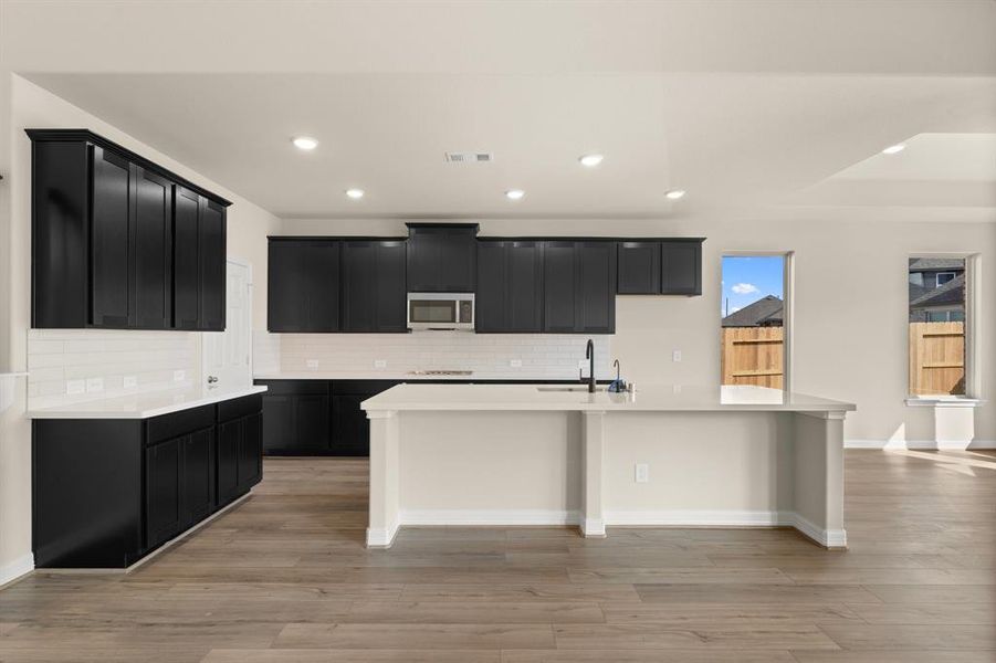 This light and bright kitchen features a large quartz island, dark stained cabinets, a large sink overlooking your family room, recessed lighting, and beautiful backsplash.