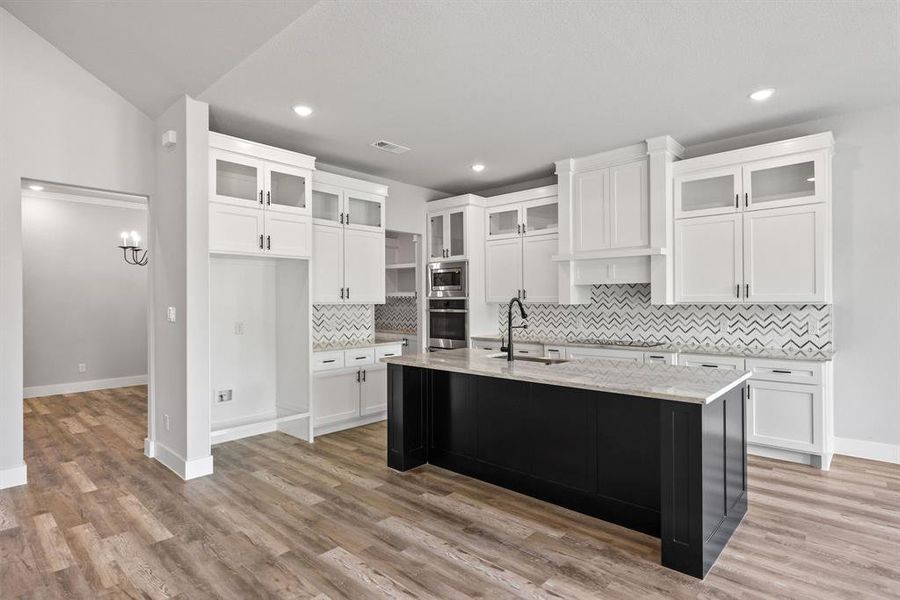 Kitchen with glass insert cabinets, light stone countertops, decorative backsplash, white cabinetry, and recessed lighting