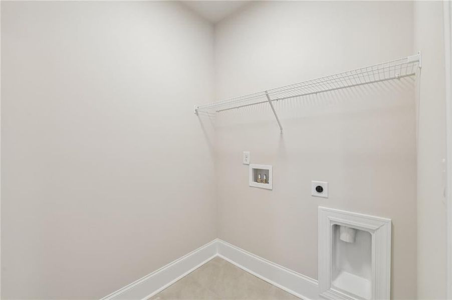 Dedicated utility space featuring light-toned walls, a wire shelving unit, tile flooring, and integrated appliance hookups