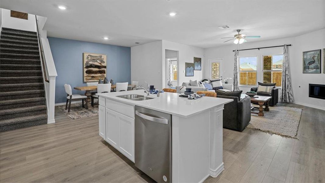 Kitchen with open floor plan, dishwasher, white cabinetry, light wood-style flooring, and an island with sink