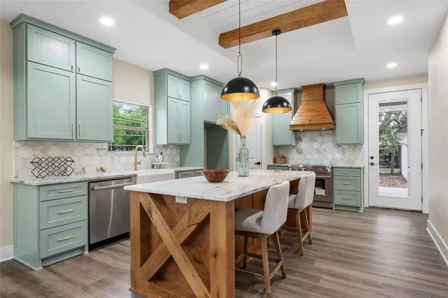 Kitchen featuring custom range hood, stainless steel appliances, green cabinets, a sink, and healthy amount of natural light