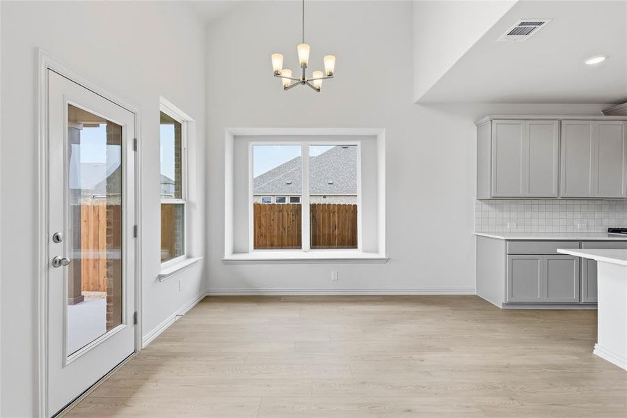 Unfurnished dining area featuring hanging lights, light wood-style floors, and a high ceiling