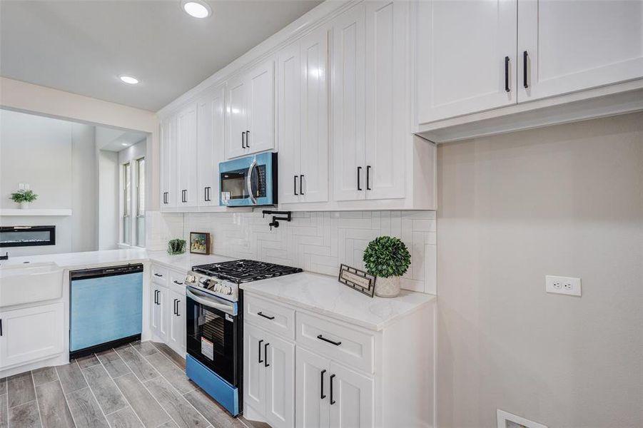 Kitchen with stainless steel appliances, backsplash, Pot filler, wood finish tile floors, white cabinets, and recessed lighting