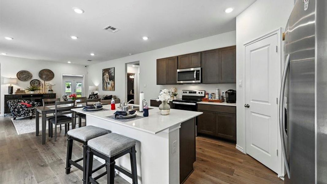 Open-concept kitchen featuring a center island with countertop seating, stainless steel appliances, dark wood-finish cabinetry, and wood-finish flooring