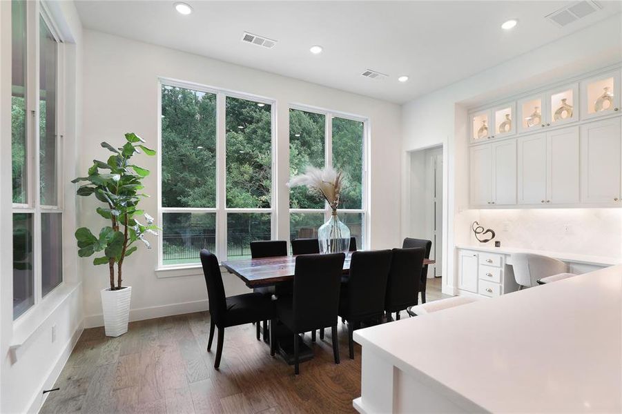 Spacious dining area featuring expansive windows, wood-finish flooring, recessed lighting, a built-in buffet with upper display cabinetry, and a dedicated desk area with under-cabinet lighting