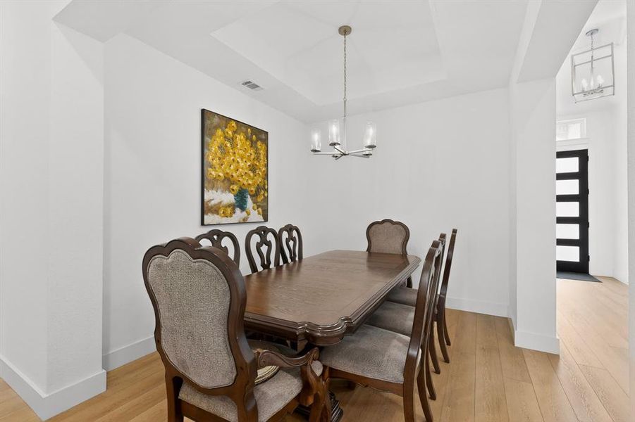 Dining area featuring a tray ceiling, a modern chandelier, and light wood-finish flooring Dining area featuring a tray ceiling, a modern chandelier, and light wood-finish flooring