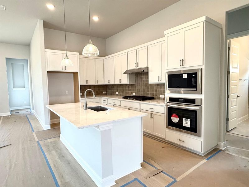 Kitchen featuring appliances with stainless steel finishes, light stone countertops, under cabinet range hood, tasteful backsplash, and white cabinets Kitchen featuring appliances with stainless steel finishes, light stone countertops, under cabinet range hood, tasteful backsplash, and white cabinets