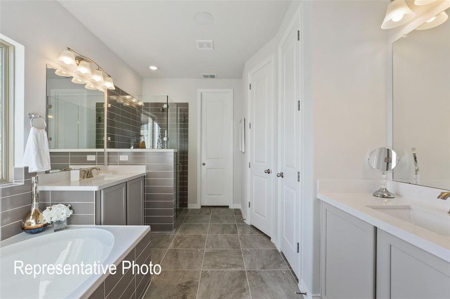 Bathroom featuring a built-in tub, dual vanities with quartz countertops, a tiled shower enclosure, and tiled flooring