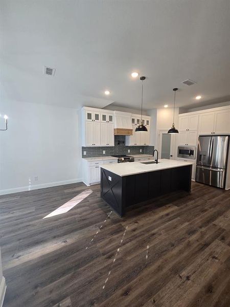 Kitchen featuring glass insert cabinets, stainless steel appliances, backsplash, hanging light fixtures, and white cabinetry