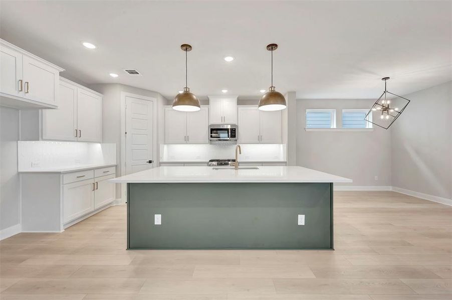 Dual tone kitchen with a center island with sink, decorative backsplash, light wood-style floors, stainless steel microwave, and dual tone cabinets