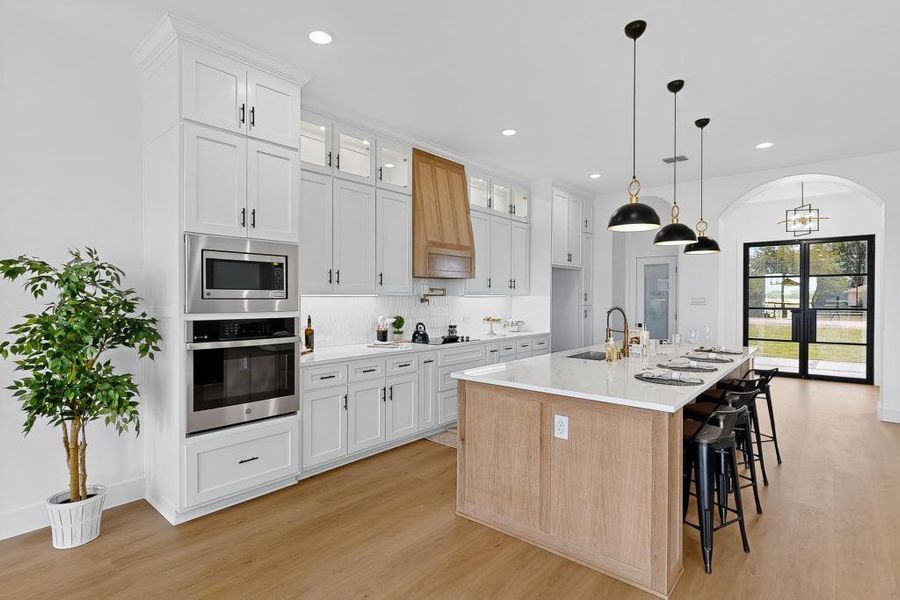 Kitchen with decorative backsplash, stainless steel appliances, arched walkways, white cabinets, and an island with sink