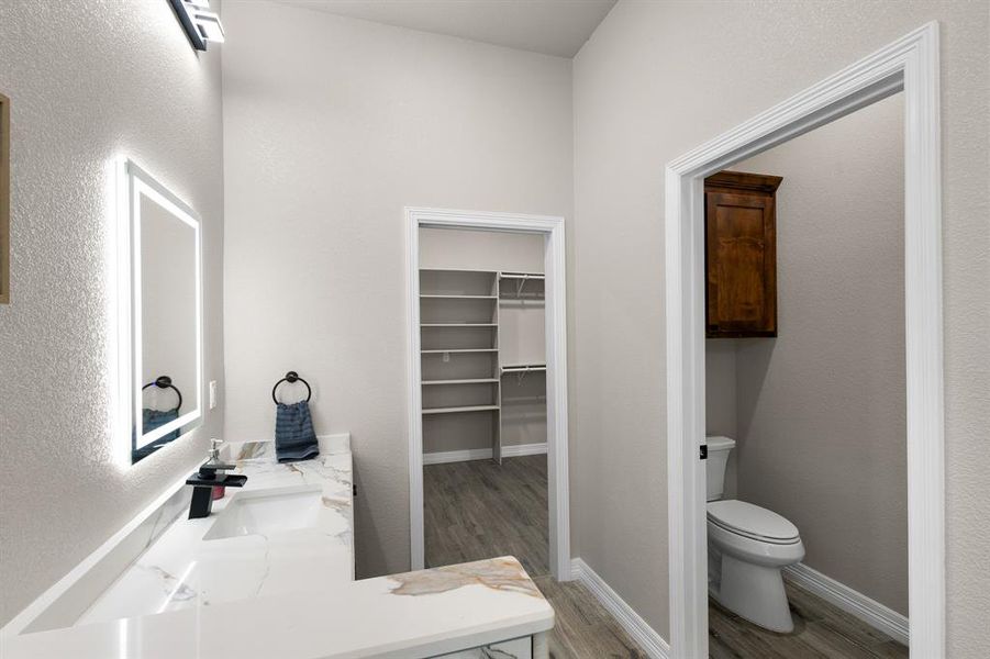 Full bath with a spacious closet, light wood-style flooring, vanity, and a textured wall