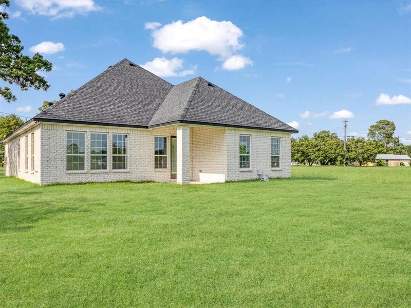 Rear view of property with a shingled roof, a yard, and brick siding