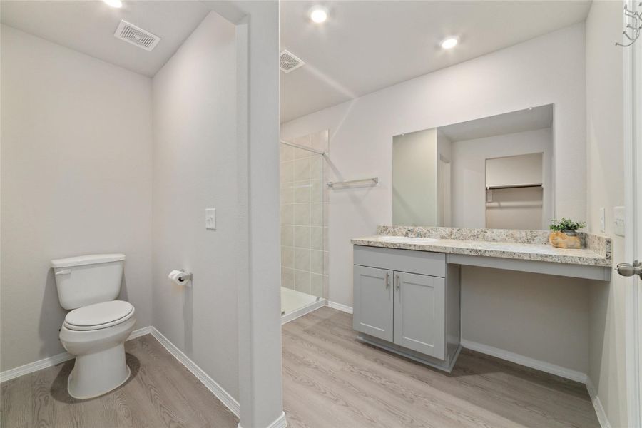 Primary bathroom with bright lighting and a clean layout, featuring a large mirror and an open feel that connects to the closet.