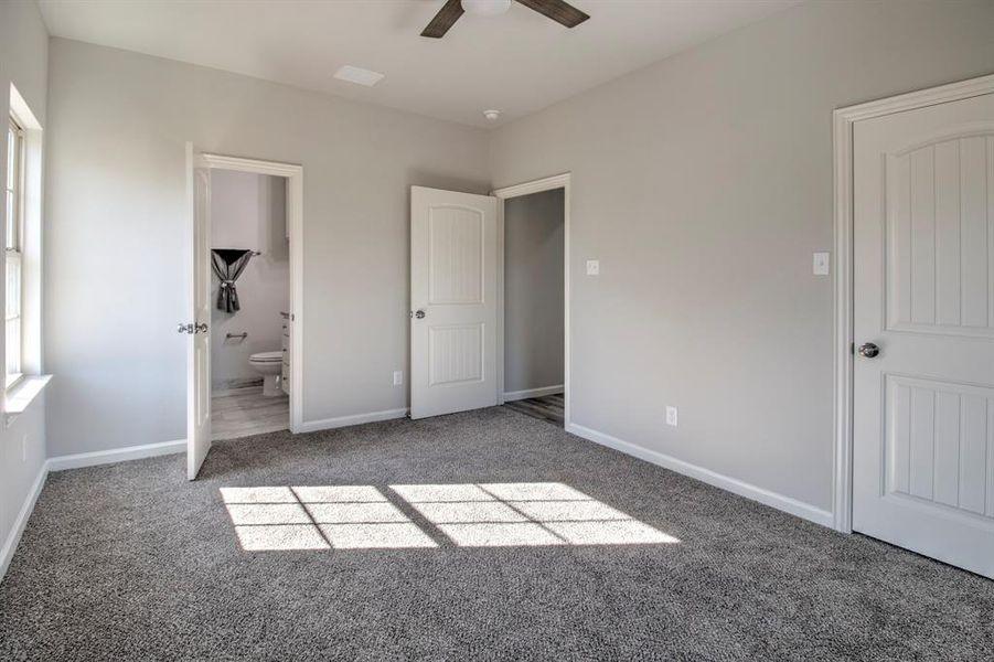 Unfurnished bedroom with ceiling fan, dark carpet, and ensuite bathroom