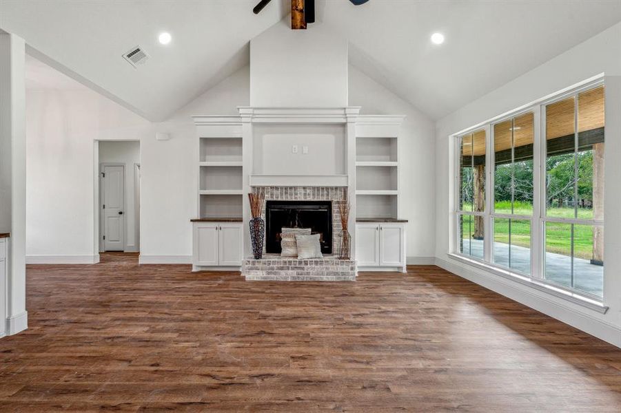 Unfurnished living room with beamed ceiling, hardwood / wood-style flooring, a brick fireplace, high vaulted ceiling, and ceiling fan