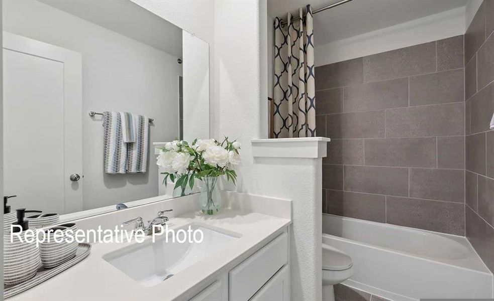 Bathroom featuring a vanity with a white countertop and an integrated sink, a rectangular mirror, and a bathtub with gray tile surround
