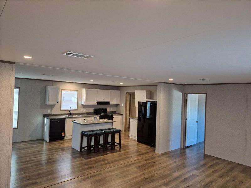 Kitchen with a kitchen island, black appliances, white cabinets, dark wood-style floors, and dark countertops
