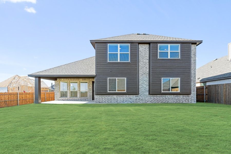 Two-story home rear view with dark siding, brick exterior, covered patio, and large green backyard