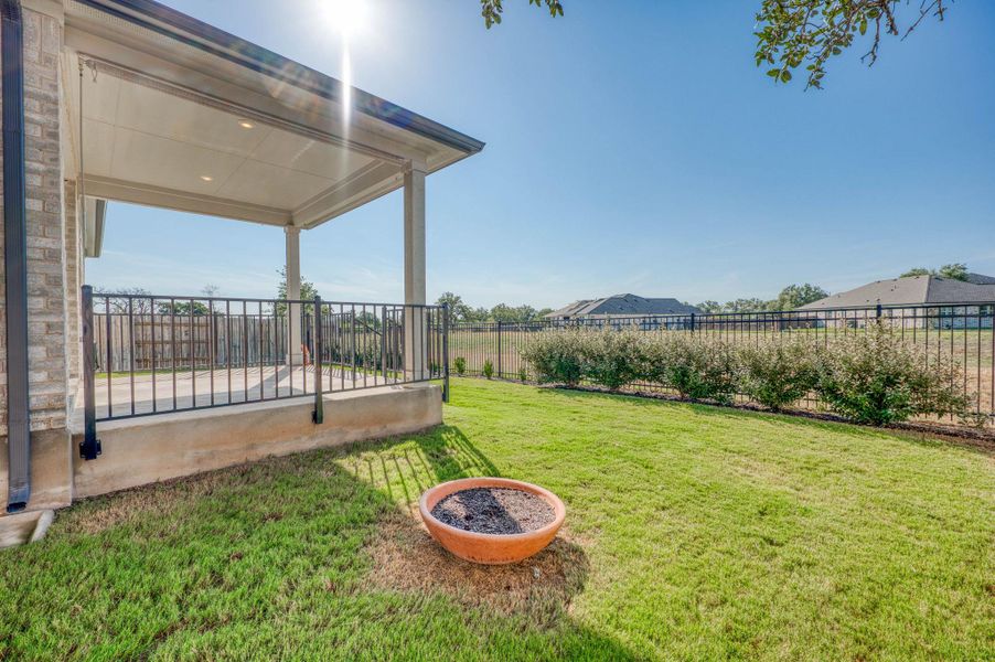 A spacious grassy yard sits framed by a wrought iron fence and covered patio.